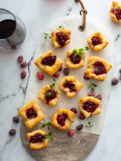 Overhead view of cranberry brie bites on a marble and wood serving board