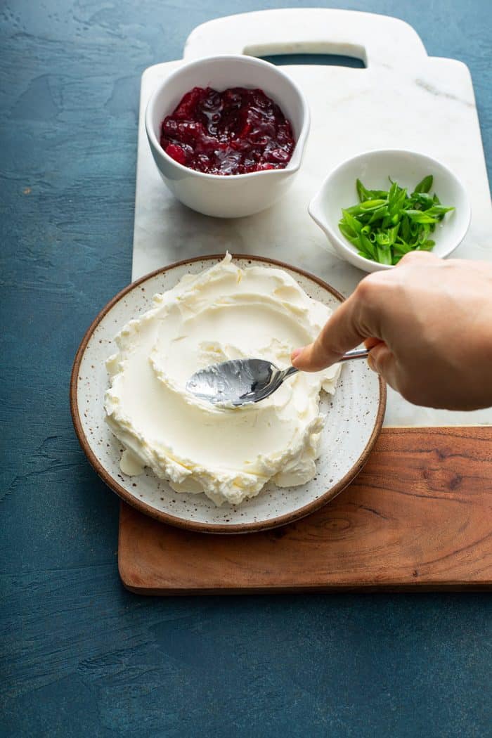 Hand using a spoon to spread softened cream cheese onto a plate