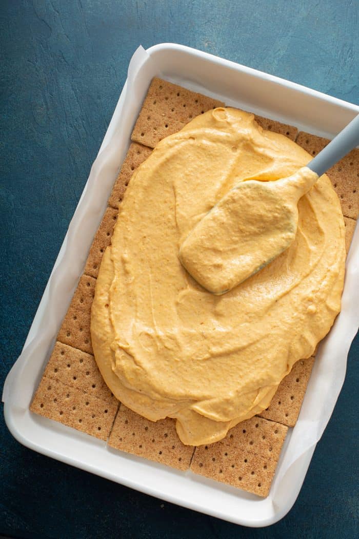 Spatula spreading pumpkin filling over graham crackers in a cake pan