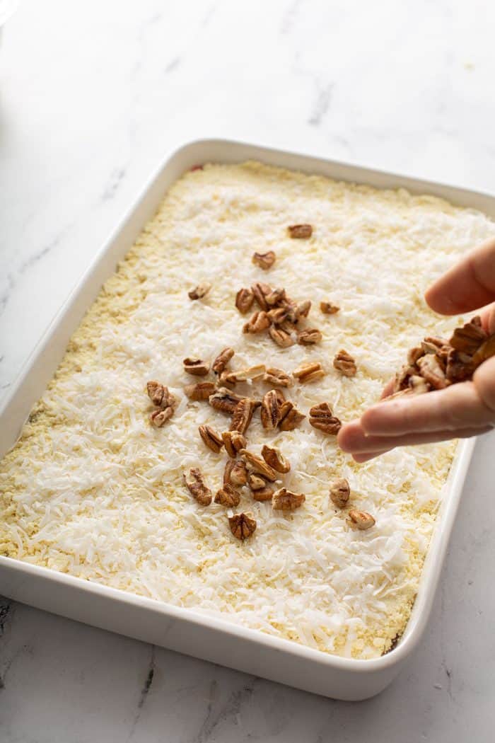 Hand sprinkling chopped pecans on top of cake mix and coconut in a cake pan