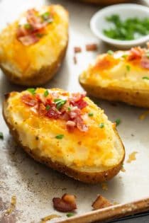 Three finished twice-baked potatoes, topped with chives and bacon, on a sheet tray