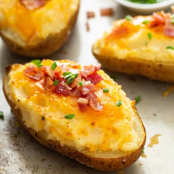 Three finished twice-baked potatoes, topped with chives and bacon, on a sheet tray