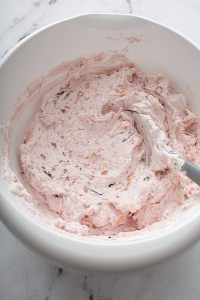 Spatula stirring together whipped topping, cranberry sauce and crushed pineapple in a mixing bowl