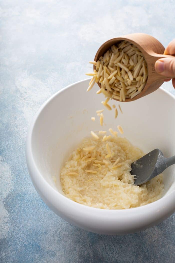 Slivered almonds being added to coconut macaroon dough in a white mixing bowl