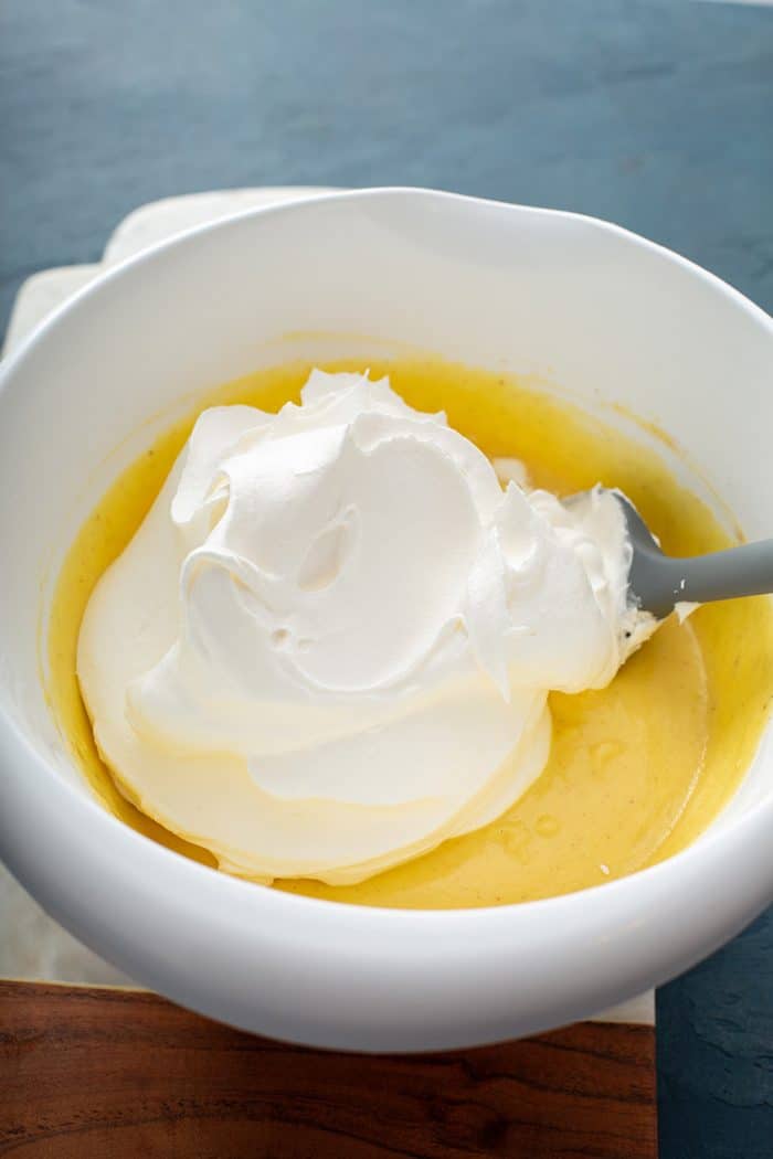 Spatula folding in whipped topping into eggnog pudding in a white mixing bowl