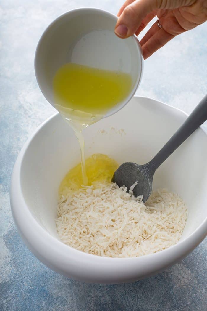 Egg whites being added to coconut in a white mixing bowl