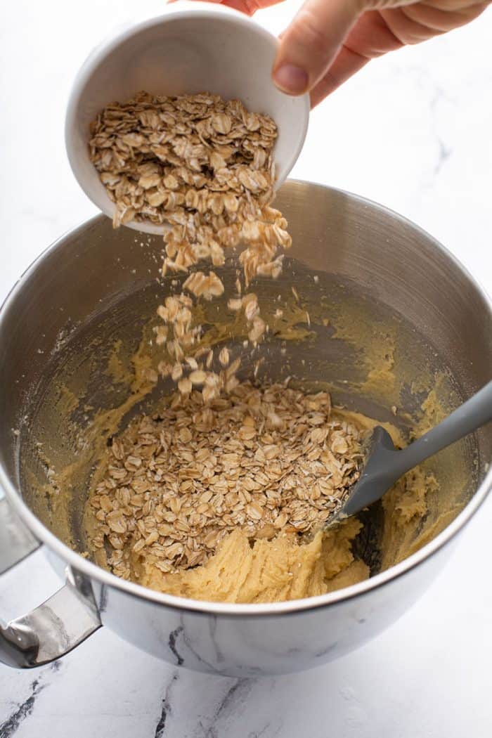 Rolled oats being added to cookie dough in a metal mixing bowl