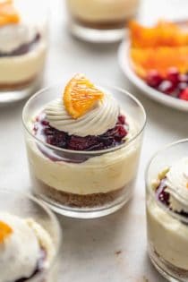 Mini cranberry cheesecake in glass dishes topped with whipped cream and a slice of orange