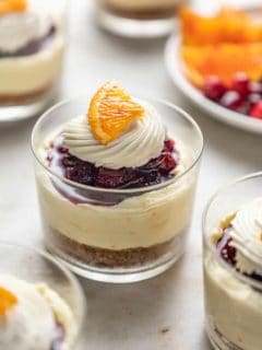 Mini cranberry cheesecake in glass dishes topped with whipped cream and a slice of orange