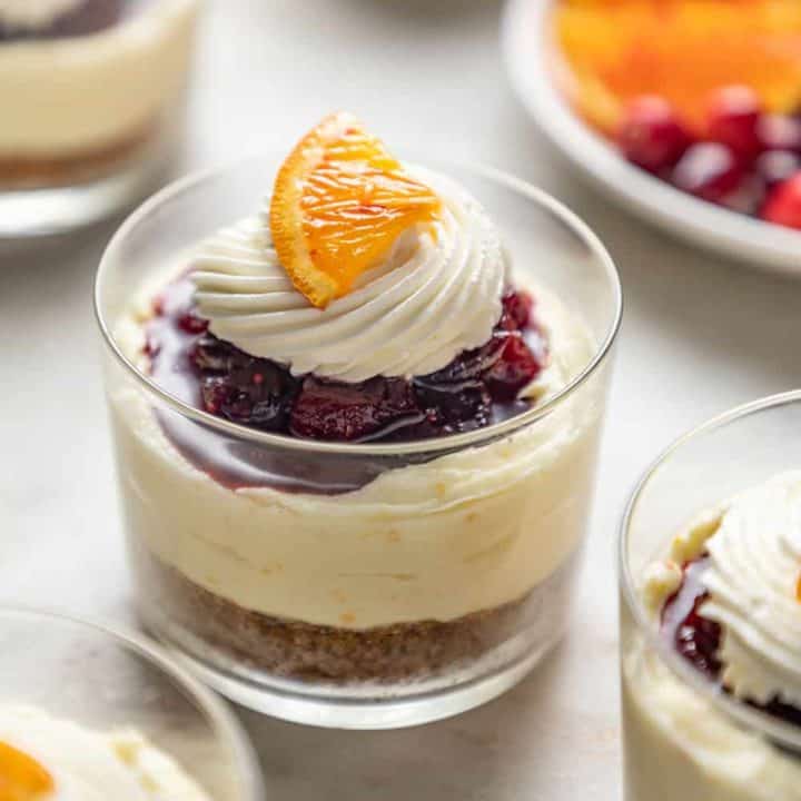 Mini cranberry cheesecake in glass dishes topped with whipped cream and a slice of orange
