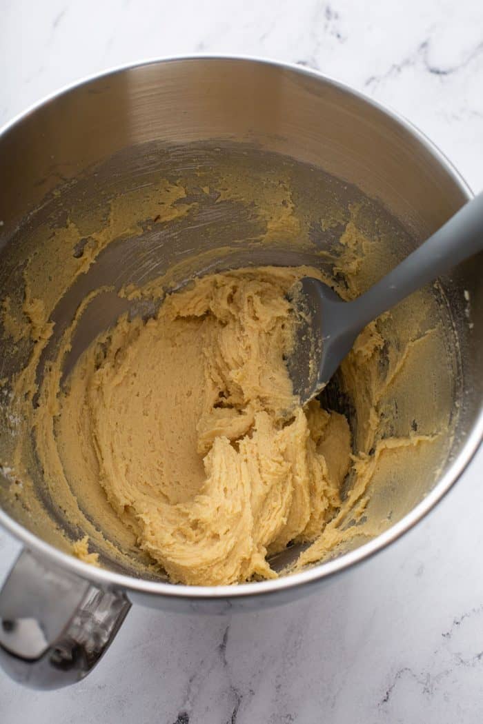 Spatula stirring together cookie dough in a metal mixing bowl