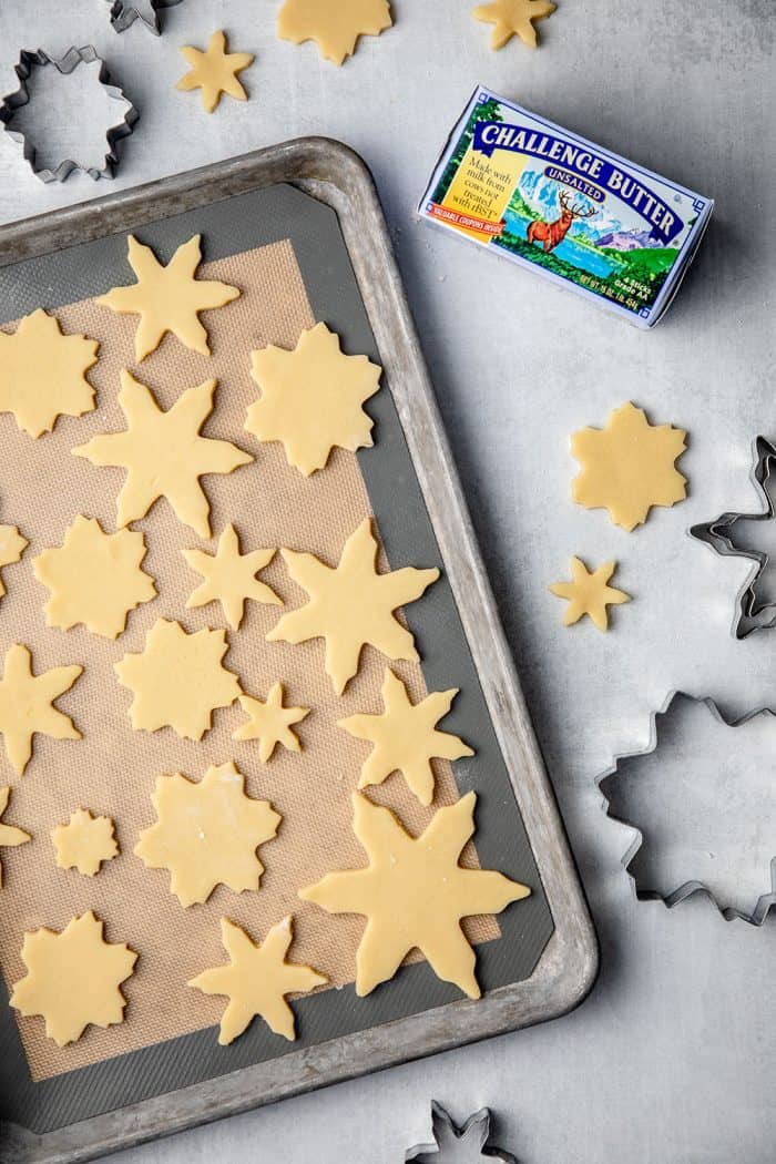 Sugar cookie dough cut into snowflake shapes on a baking sheet, ready to bake
