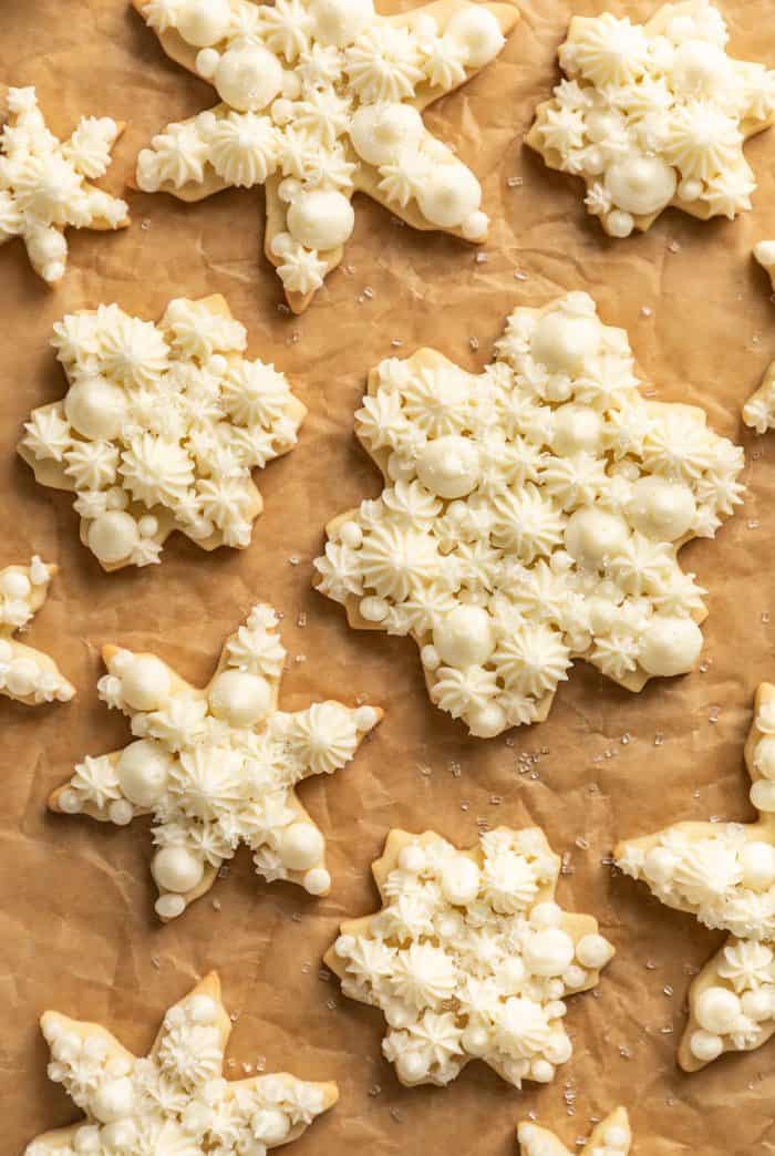 Snowflake sugar cookies decorated with buttercream frosting arranged on a piece of parchment paper