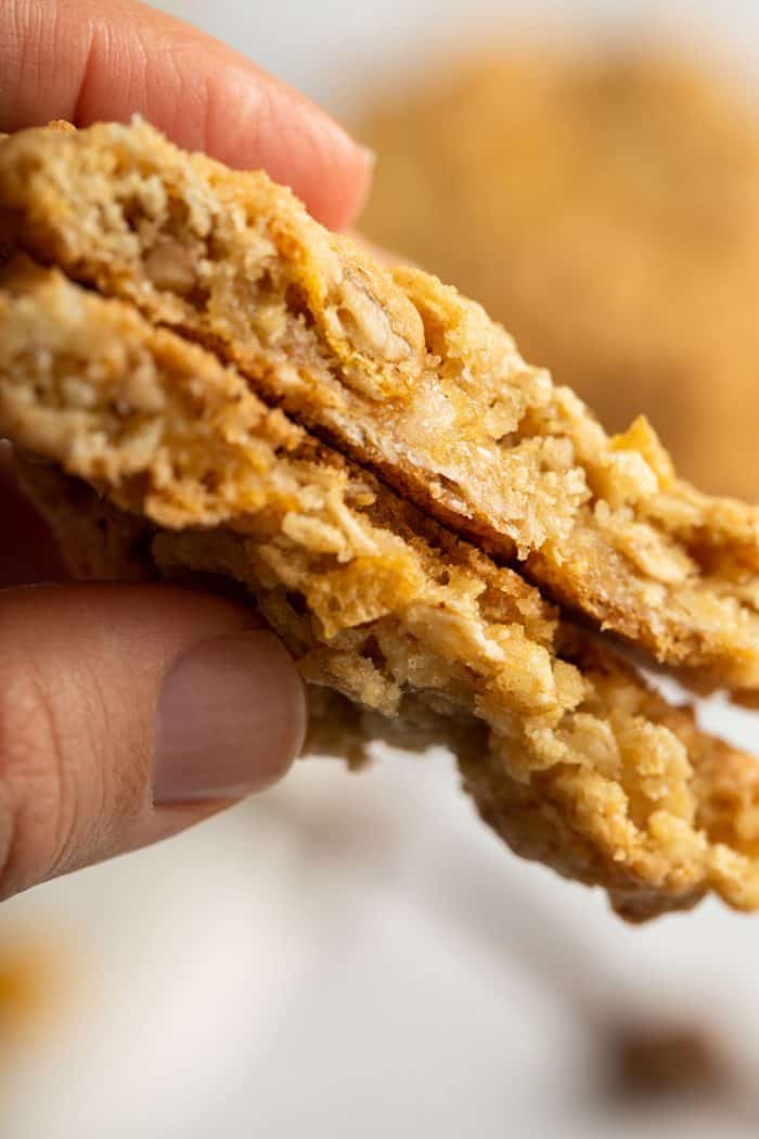 Hand holding up two halves of a cornflake cookie to show the texture of the cookie