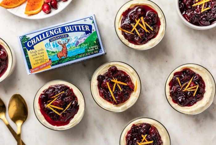 Mini cranberry cheesecakes topped with cranberry sauce on a marble counter next to a package of butter
