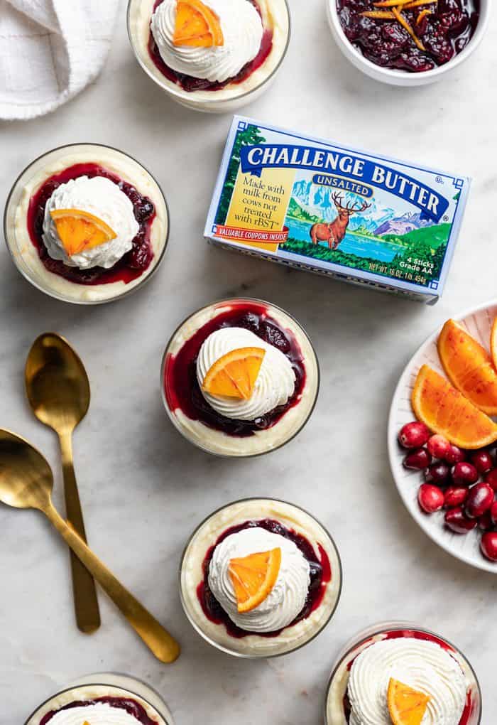 Overhead view of five mini cranberry cheesecakes topped with whipped cream and an orange slice on a marble counter