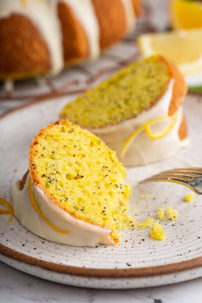 Two slices of citrus poppyseed cake on a white plate next to a fork
