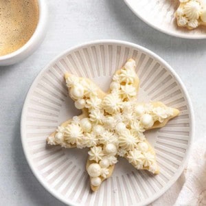 Snowflake sugar cookie on a white plate next to a cup of coffee