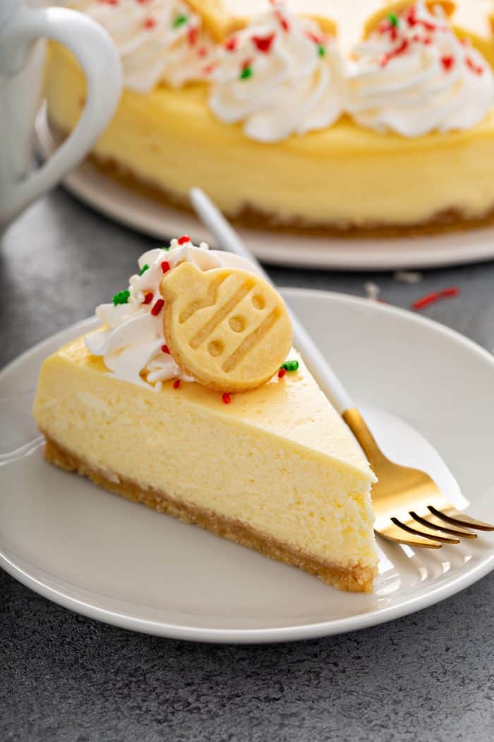 Slice of sugar cookie cheesecake next to a fork on a white plate