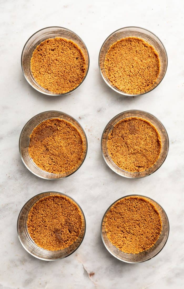 Gingersnap cookie crusts in the bottom of six glass containers lined up on a marble countertop