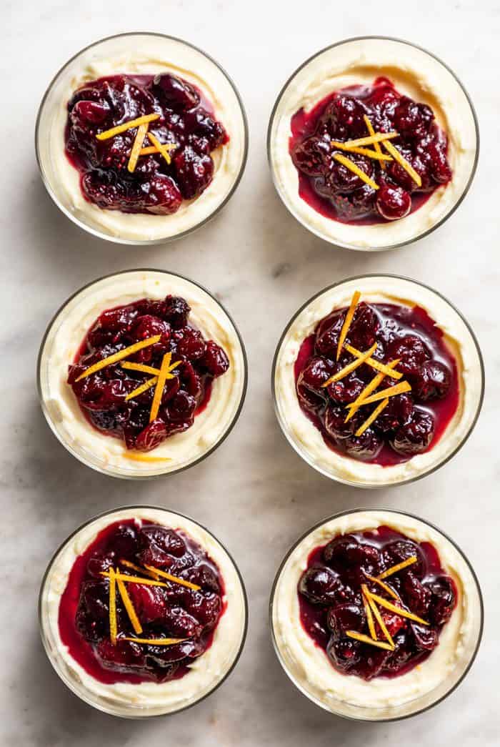 Six no-bake cranberry cheesecakes in glass dishes lined up on a marble counter