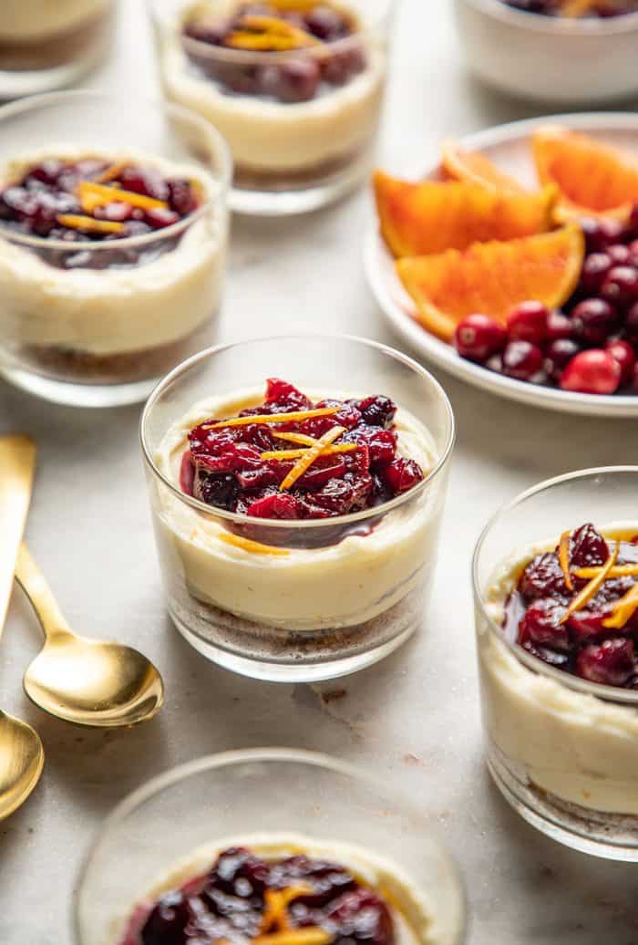 Cranberry cheesecakes topped with cranberry sauce and orange zest on a marble counter