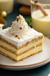 Slice of eggnog eclair cake topped with whipped cream and sparkling sugar on a white plate
