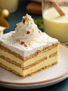 Slice of eggnog eclair cake topped with whipped cream and sparkling sugar on a white plate