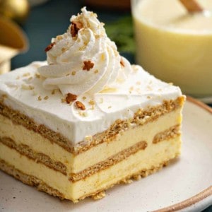 Slice of eggnog eclair cake topped with whipped cream and sparkling sugar on a white plate