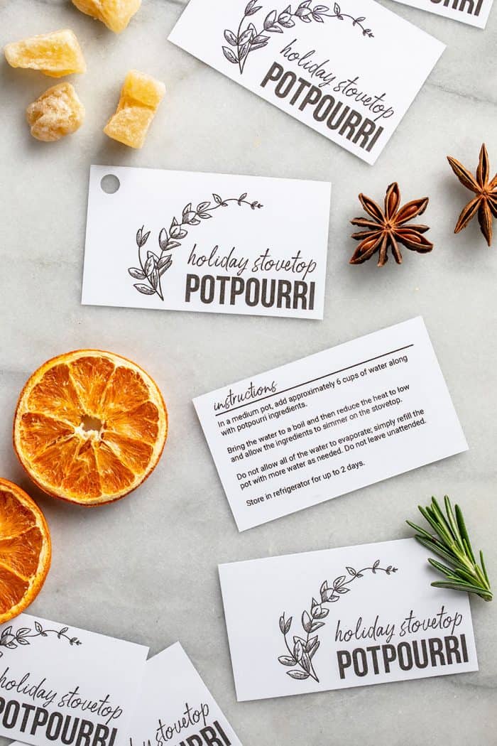 Printable holiday stovetop potpourri gift tags laid out on a counter with dried oranges and spices