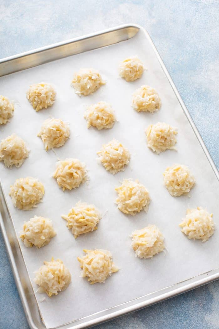 Unbaked coconut macaroons lined up on a parchment-lined baking sheet