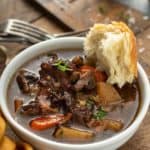 Crusty bread dipped into a bowl of beef and barley stew