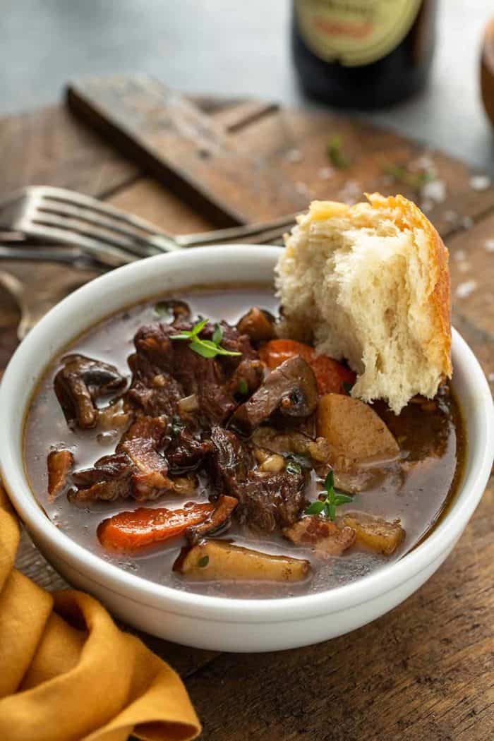 Crusty bread dipped into a bowl of beef and barley stew