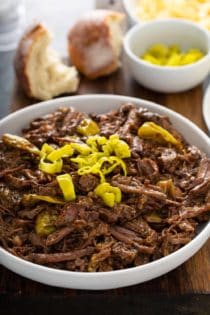 Mississippi pot roast topped with sliced pepperoncini peppers in a white serving bowl
