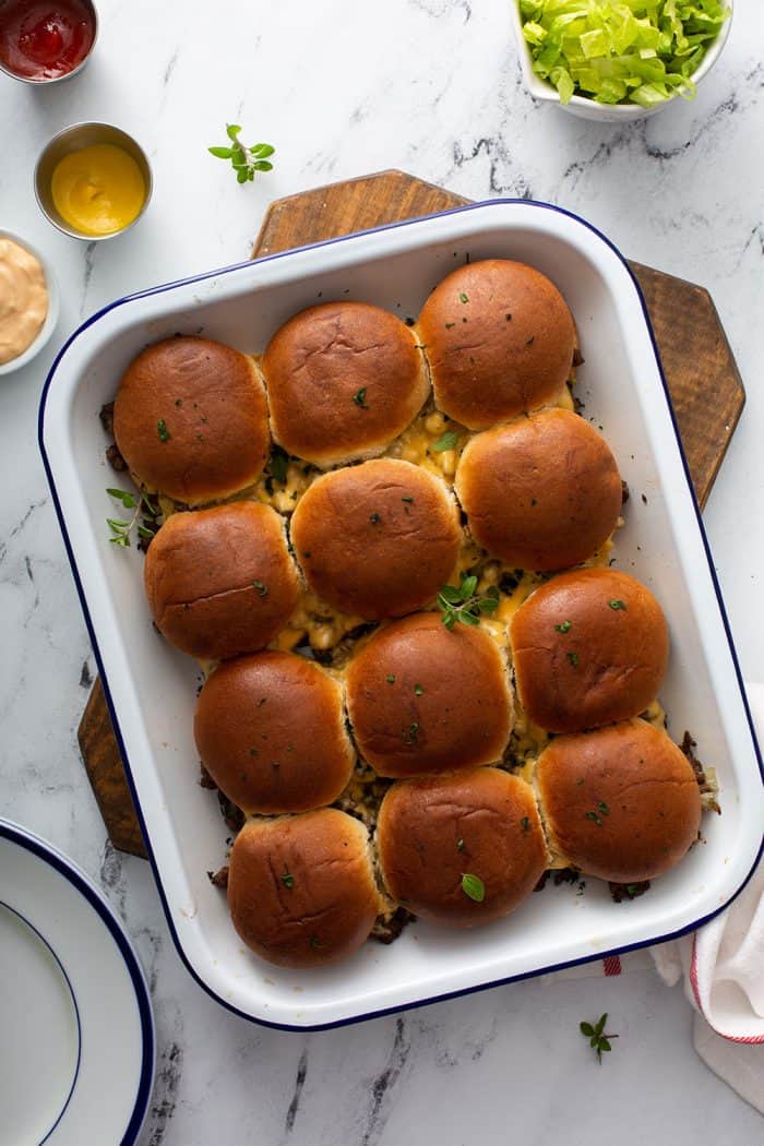 Cooked cheeseburger sliders in a white baking dish on a wooden trivet