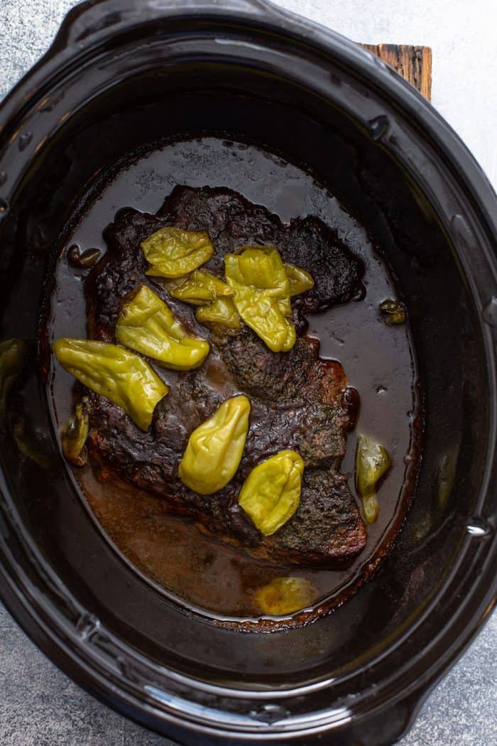 Cooked whole Mississippi topped with pepperoncinis in the crock of a slow cooker
