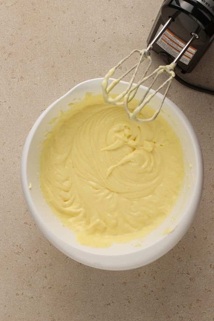 Eggs adding to the batter for cream cheese pound cake, in a white bowl.