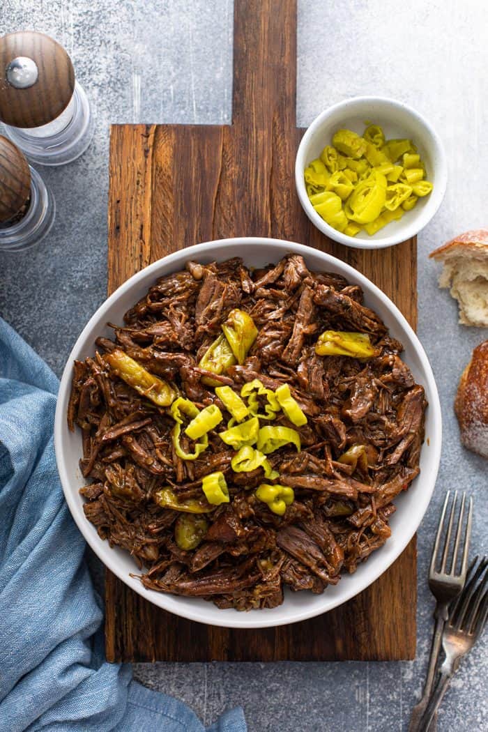 Overhead shot of shredded Mississippi roast in a white bowl, topped with sliced pepperoncini peppers