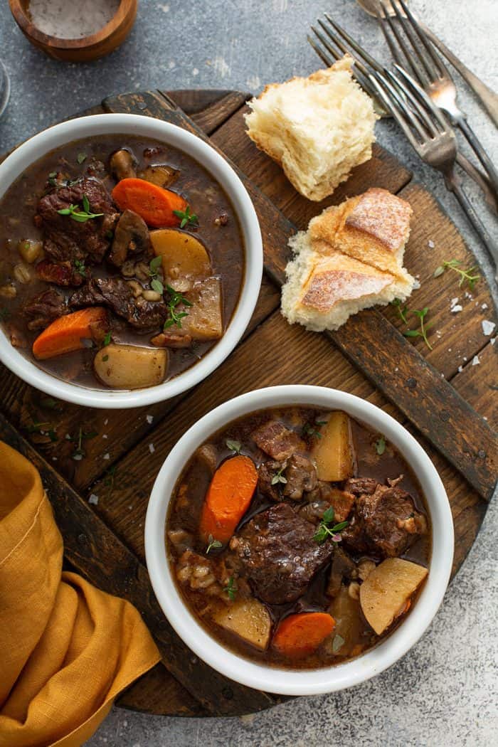 Overhead shot of two white bowls filled with beef and barley stew on a wooden cutting board