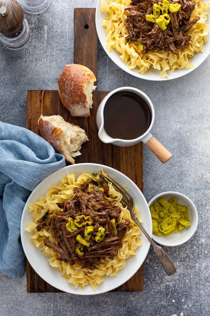 Overhead shot of two white bowls filled with Mississippi pot roast on top of egg noodles