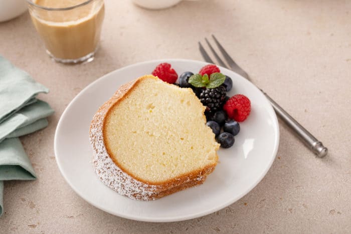 White plate with a slice of cream cheese pound cake next to mixed fresh berries.