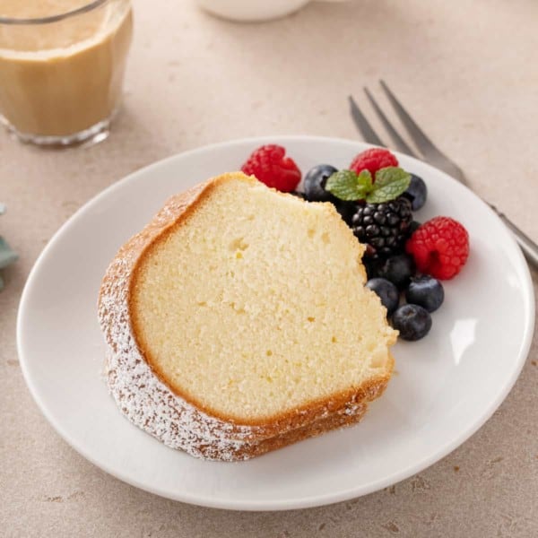 Slice of cream cheese pound cake next to fresh berries on a white plate.