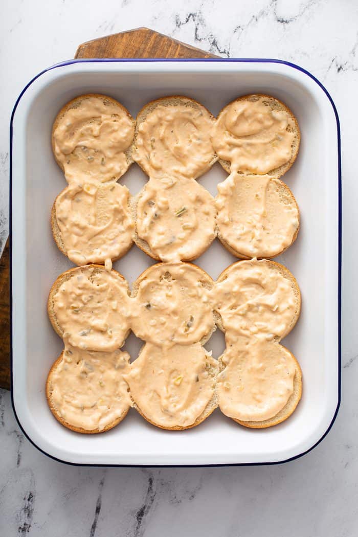 Slider bun bottoms topped with burger sauce in a white baking dish