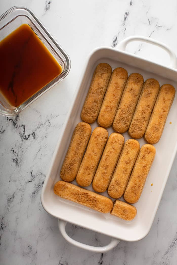 Coffee-soaked ladyfingers in a white baking dish next to a dish of coffee