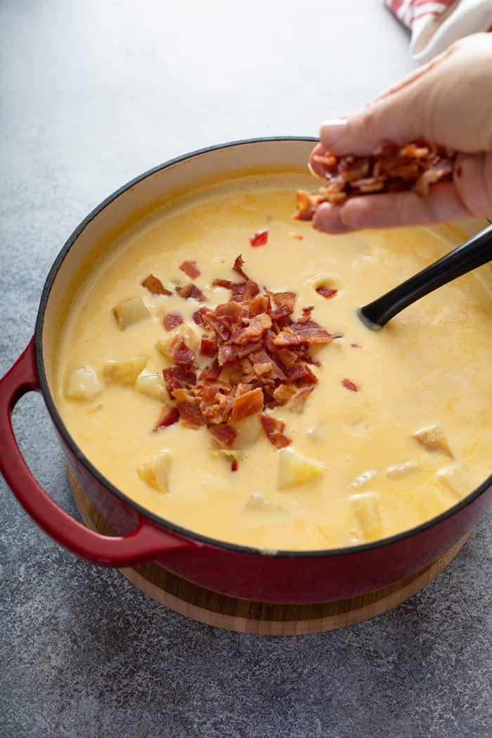 Hand adding cooked and crumbled bacon to a pot of potato soup