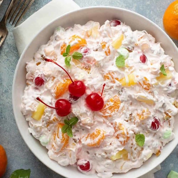 Ambrosia Salad in a white serving bowl, garnished with maraschino cherries