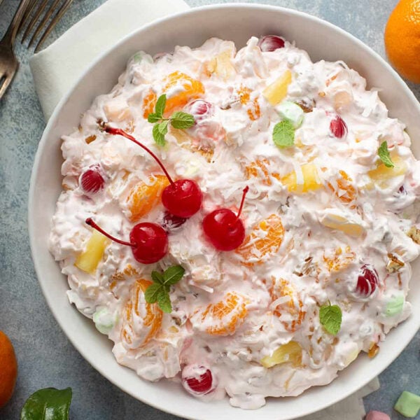 Ambrosia Salad in a white serving bowl, garnished with maraschino cherries