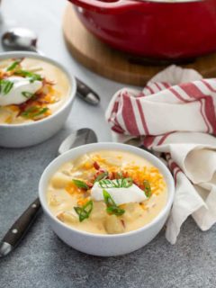 Baked potato soup in a white bowl, topped with sour cream and green onions