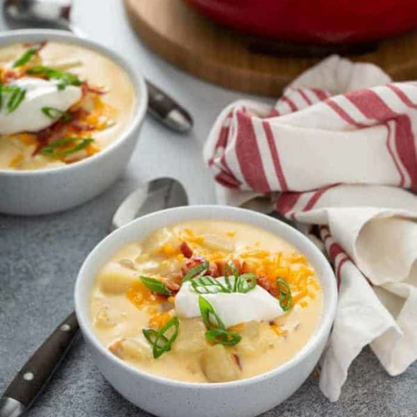 Baked potato soup in a white bowl, topped with sour cream and green onions