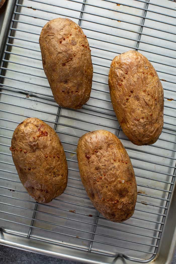 Four baked potatoes on a wire rack
